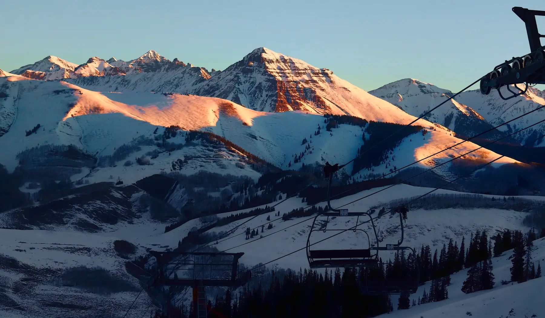 Ski lift climbing the mountain with snowy peaks, morning light